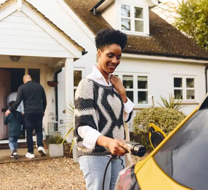 Woman smiling outside house with family entering doorway