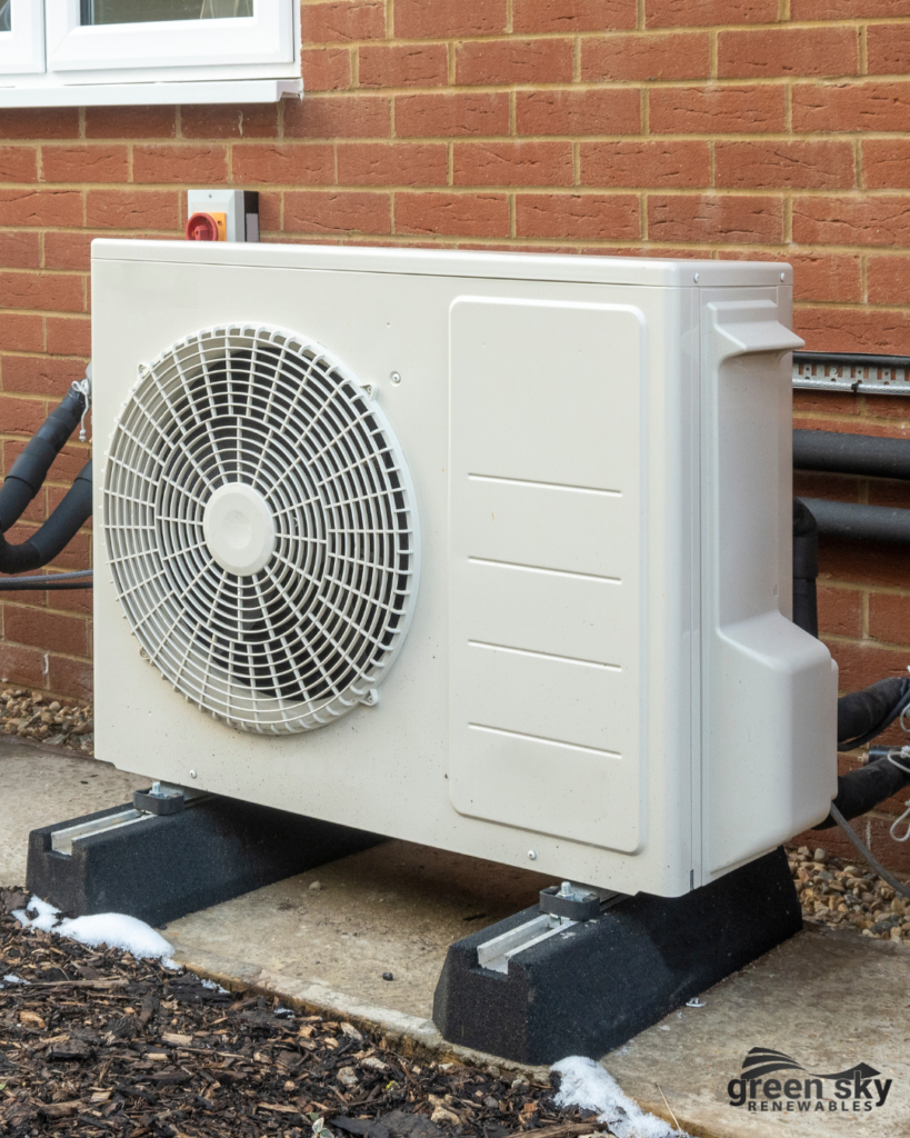 White heat pump unit mounted on brick wall outdoors